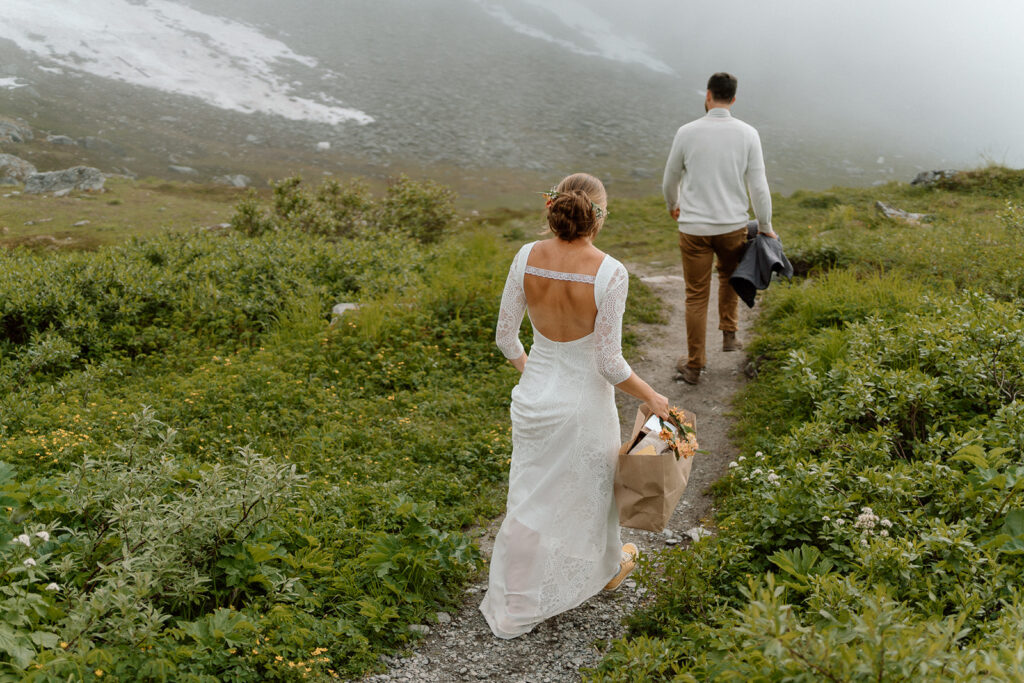 couple holding bags and walking to their elopement ceremony in the mountains in Alaska
