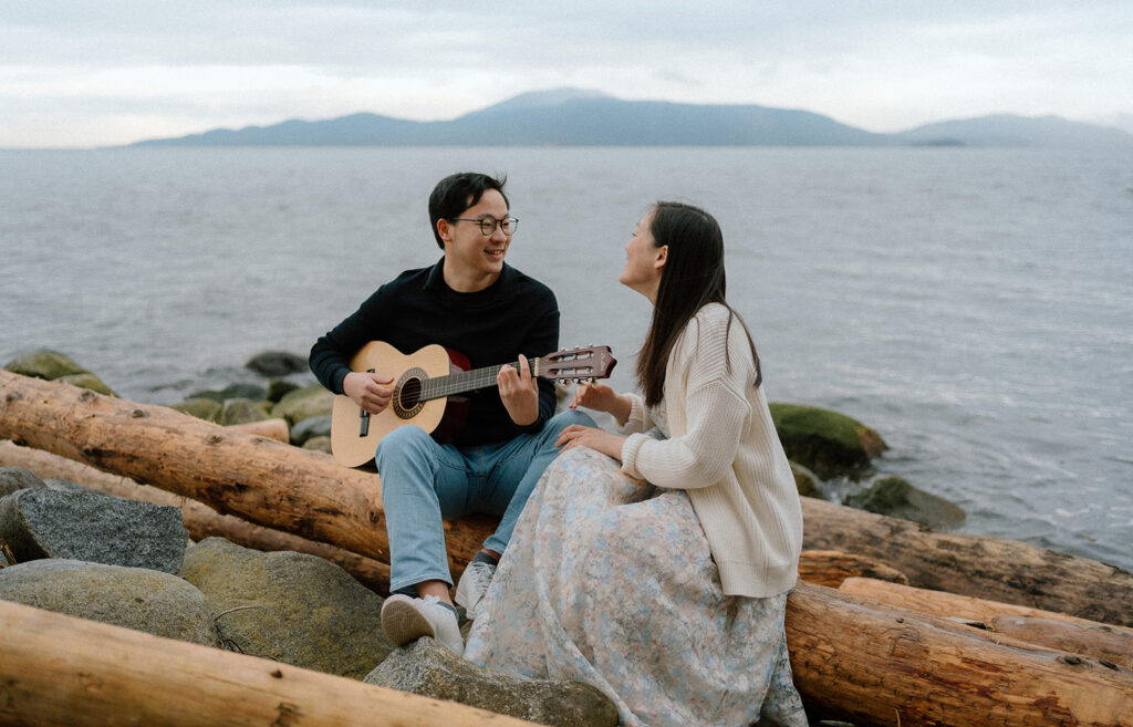 engaged couple sitting at a beach and playing guitar