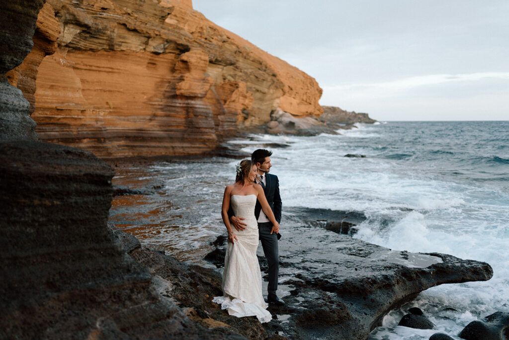 photographer photographs couple in wedding attire in a cave overlooking the ocean