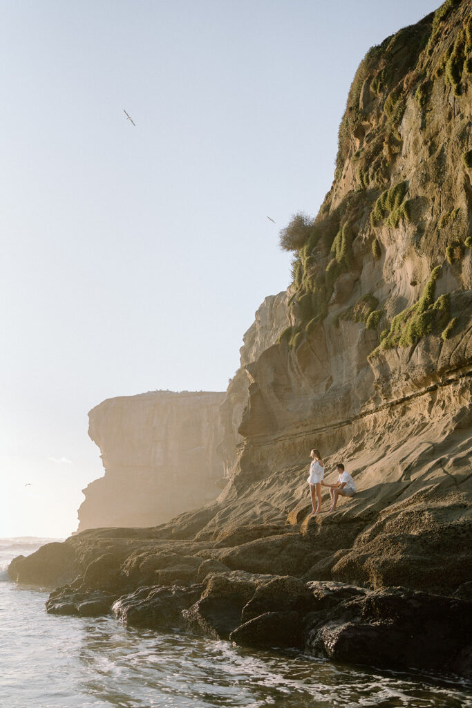 Couple sitting in rocky cliffs by the ocean in New Zealand overlooking the water 