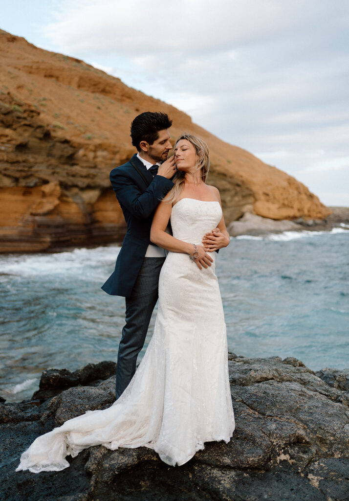 destination elopement photographer captures couple hugging by orange rocky cove and the ocean in Playa Amarilla in the Canary Islands